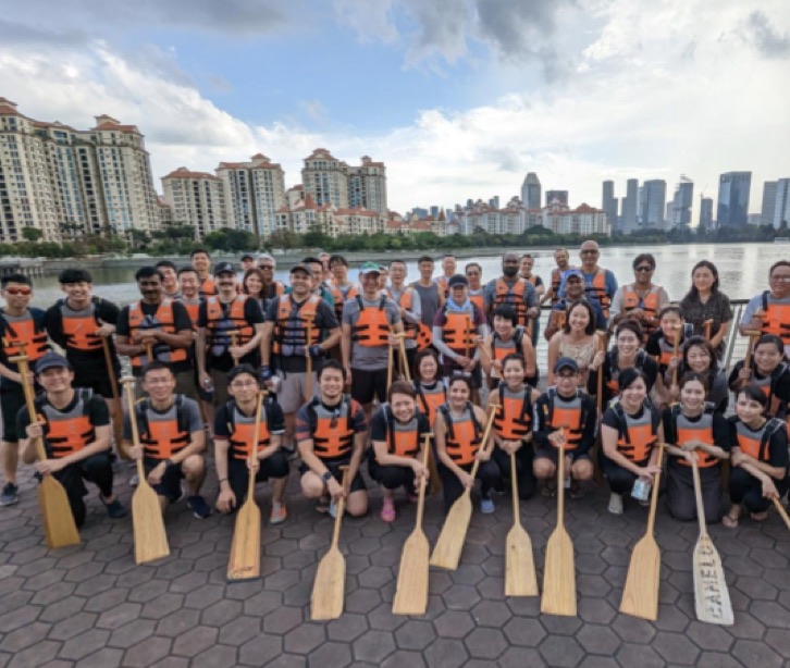 湖を背景にライフジャケットを着てボート用パドルを持つ社員の一行